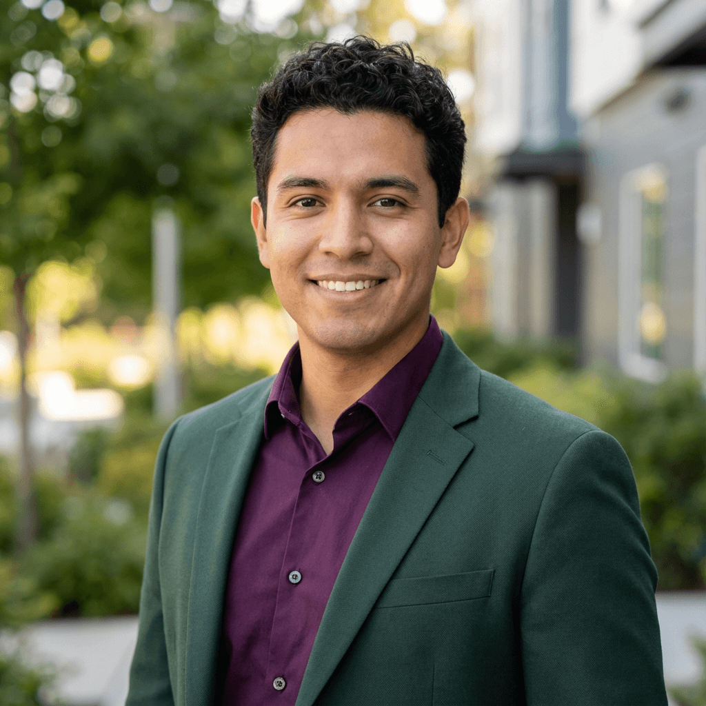 Hombre sonriente con cabello rizado, vistiendo un blazer verde y camisa morada en exteriores.